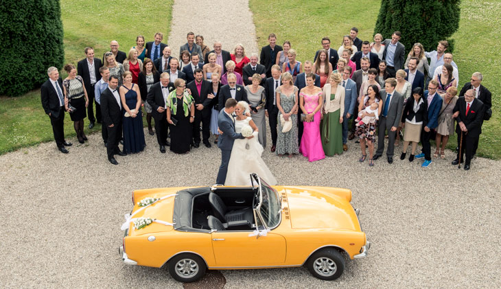 brudepar krammer foran gæster og bryllupsvogn